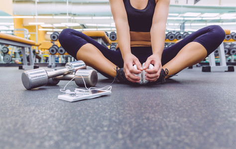 Sporty woman sitting with dumbbells and smartphone in gym floor
