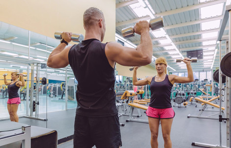 Man coach training to woman with dumbbells exercises