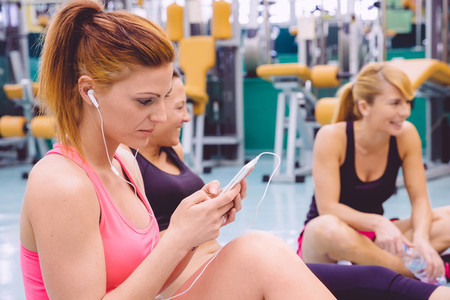 Woman listening music in smartphone and friends talking on the gym