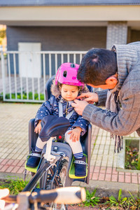 Father closing helmet to her daughter sitting in bike seat