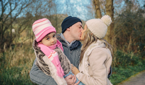 Happy couple with daughter kissing in the forest