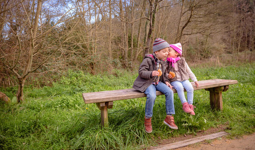 Little girl talking to the ear of boy sitting on bench