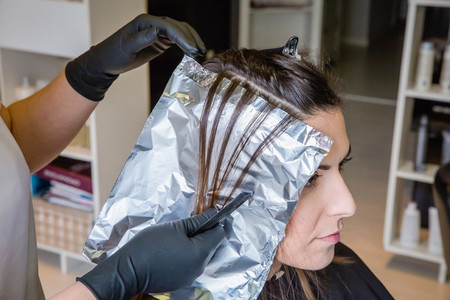 Hairdresser hands separating woman hair with aluminium foil