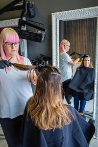 Hairdresser with black gloves combing hair of woman