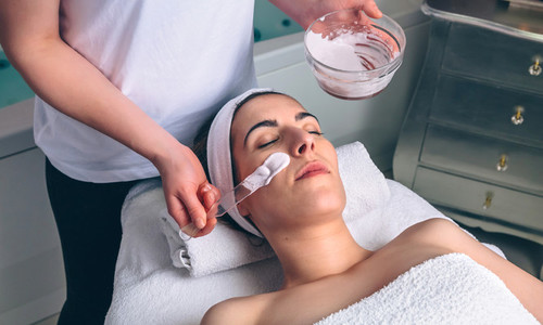 Woman receiving facial mask from beautician in spa