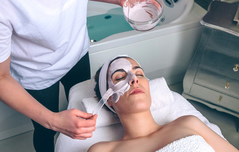 Beautician applying facial mask to woman in spa