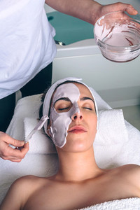 Beautician applying facial mask to woman in spa