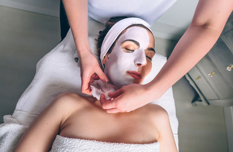 Beautician removing facial mask to woman in spa