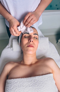 Beautician removing facial mask to woman in spa