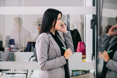 A businesswoman talking by cellphone near a window in the office