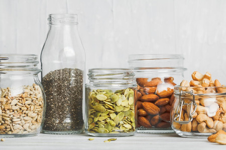 Various nuts and seeds in glass jars over white wooden table against white background  The concept of vegetarian and organic food  Set of photos