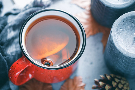 Winter season hot tea in a red ceramic mug surrounded by black aromatic candles  warm scarf  maple leaves on a concrete grey background  The concept of cosy holidays and New Year