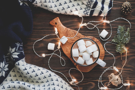 Hot cocoa with marshmallow in a white ceramic mug surrounded by winter things on a wooden table  The concept of cosy holidays and New Year  Top view  flat lay
