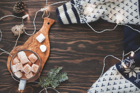 Hot cocoa with marshmallow in a white ceramic mug surrounded by winter things on a wooden table  The concept of cosy holidays and New Year  Top view  flat lay