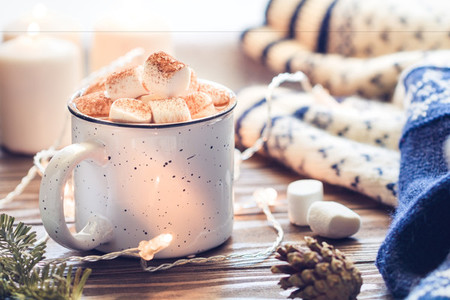 Hot cocoa with marshmallow in a white ceramic mug surrounded by winter things on a wooden table  The concept of cosy holidays and New Year