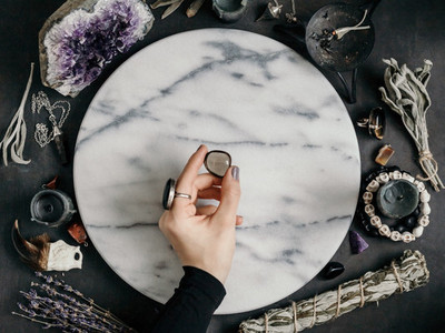 Witchs hand holding Smoky quartz above a marble white round tray  The place for witchcraft with magic things around  View from above