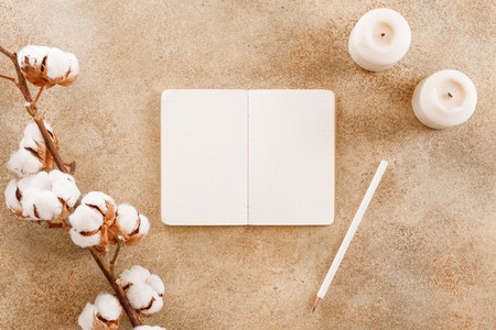 Open notebook with white pencil among cotton flowers branch and white candles  Flat lay  top view  cmock up  The concept of planning and goals to set on New Year