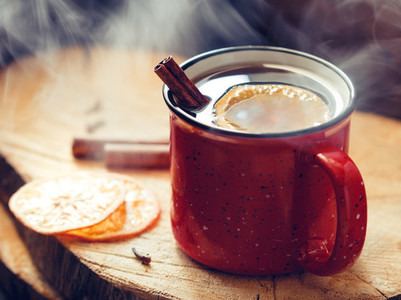 Mulled wine in a red ceramic mug over rustic wooden boards surrounded spices
