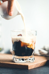 Hand is pouring milk in a glass with espresso and iced cubes