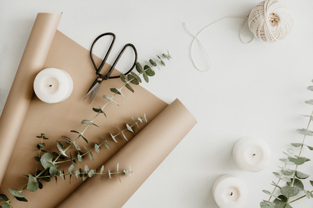 Creating of a bouquet with baby blue eucalyptus branch in a golden wrapping paper among white candles on a table  The concept of a florist work or celebration  Top view  flat lay