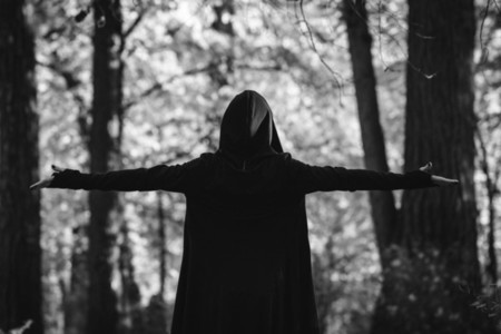 View from the back on a black witch in a mantle during ritual in a forest  Black and white moody photography  The concept of Halloween and witchcraft