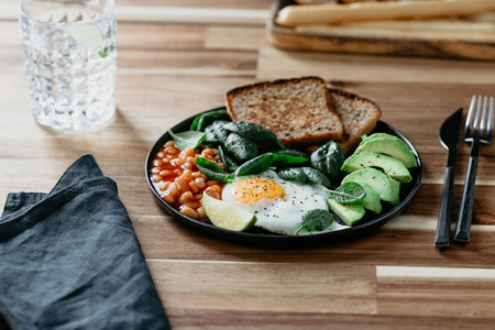 Healthy breakfast or lunch at home or cafe with fried egg  avocado  toasts  beans and fresh spinach on a wooden table