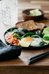 Healthy breakfast or lunch at home or cafe with fried egg avocado toasts beans and fresh spinach on a wooden table