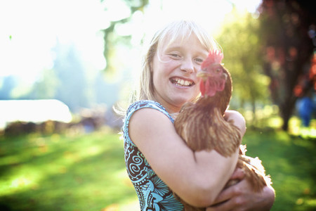 Portrait happy girl holding hen in sunny yard