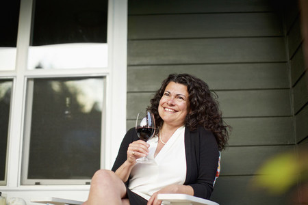 Happy woman drinking red wine on front porch
