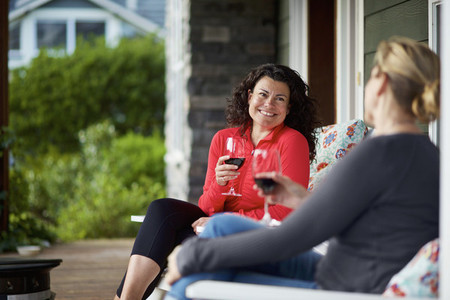 Happy women talking and drinking red wine on front porch