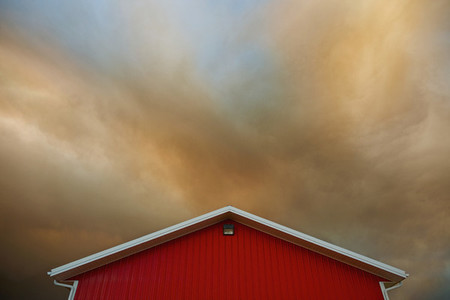Orange clouds forming in dramatic sky over vibrant red barn