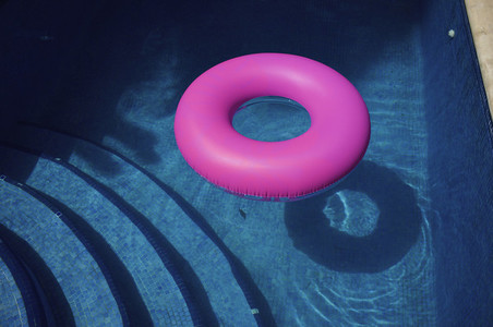Bright pink inflatable ring in sunny blue swimming pool