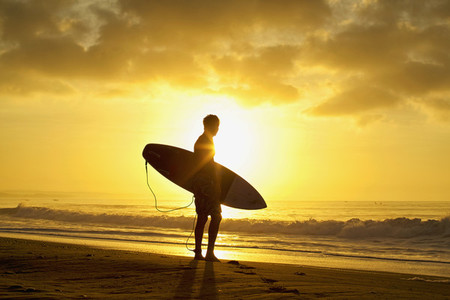 Silhouetted male surfer with surfboard on tranquil