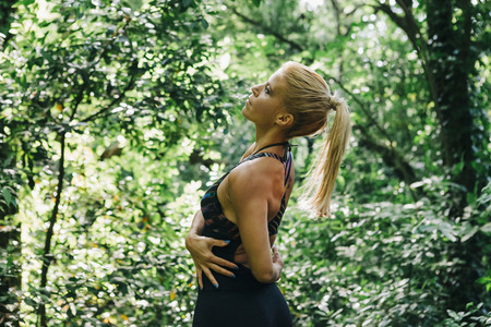 Fit female personal trainer stretching in forest