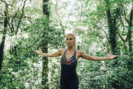 Fit female personal trainer exercising stretching arms in forest