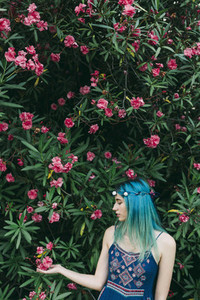 Serene young woman with blue hair standing below flowering tree