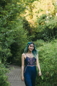Portrait smiling happy young woman with blue hair walking along footpath in lush park