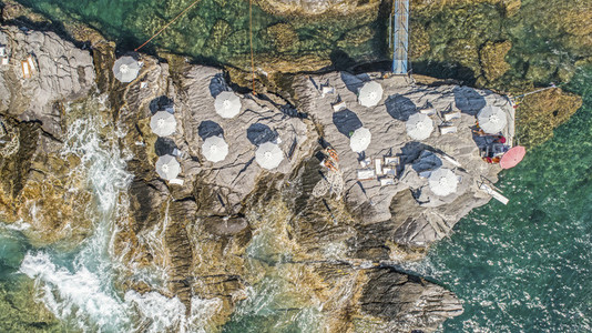 Aerial view from above beach umbrellas on sunny rocks above ocean