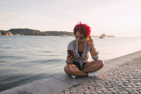 Woman with red hair listening to music with headphones and smart phone at waterfront