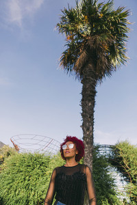 Stylish woman wearing sunglasses below sunny palm tree