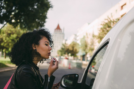 Young woman applying lip gloss in van window
