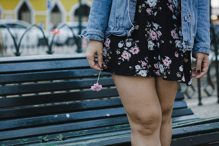 Cropped image woman in floral dress holding flower at park bench