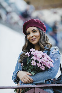 Portrait smiling young woman in beret holding flower bouquet