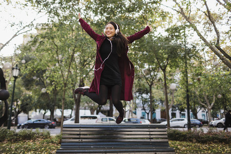 Portrait playful exuberant woman jumping off urban city bench