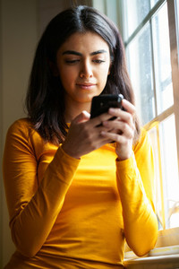 Persian woman using her smart phone near the window