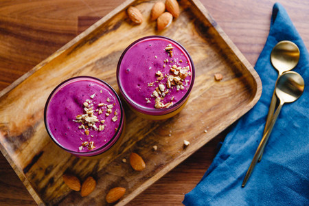 Top view of two glasses with violet berry smoothie are served crushed almond on a wooden tray