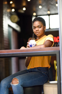Smiling black woman with very short hair drinking a cocktail in an urban cafe