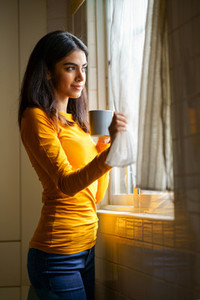 Persian woman drinking coffee while looking through the window