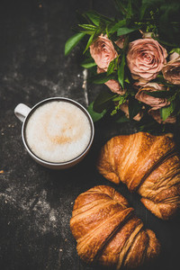 Cup of cappuccino  fresh croissants and pink flowers  top view