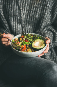 Woman in sweater eating healthy vegetarian dinner from Buddha bowl